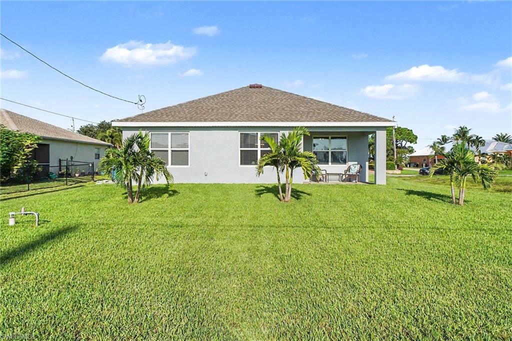Expansive rear yard featuring mature tropical plantings, a covered patio, and multiple large windows