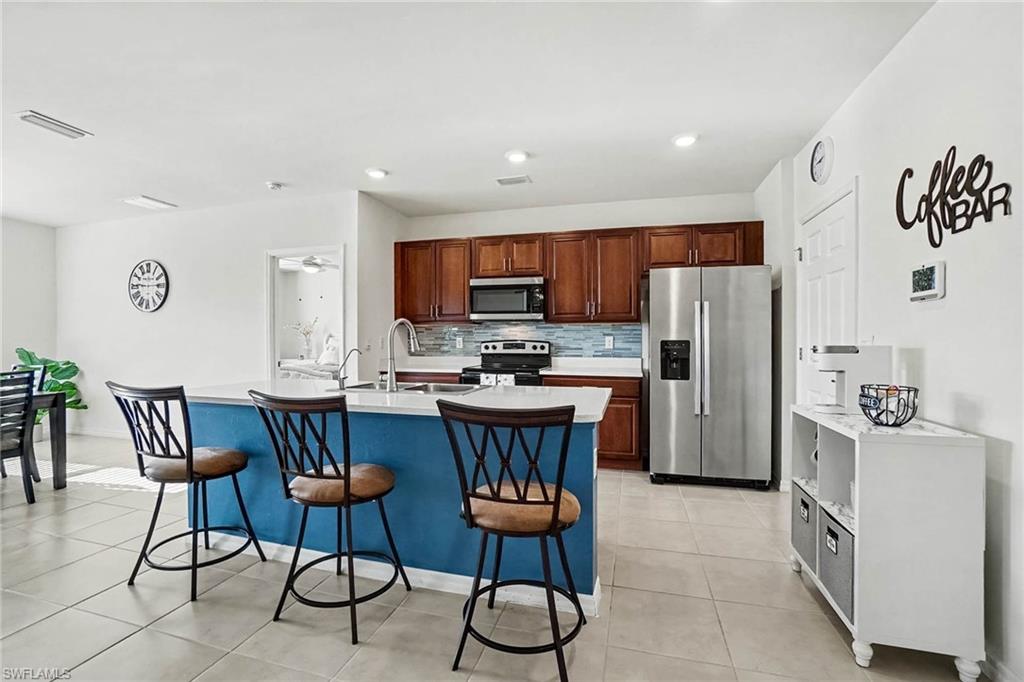 Open-concept kitchen featuring an island with a breakfast bar, stainless steel appliances, wood cabinetry, and tile flooring