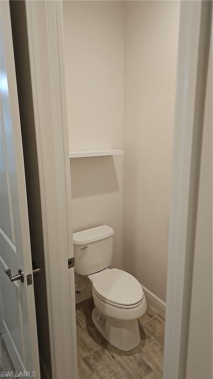Compact powder room featuring a contemporary two-piece toilet, wood-finish tile flooring, and a built-in wall shelf