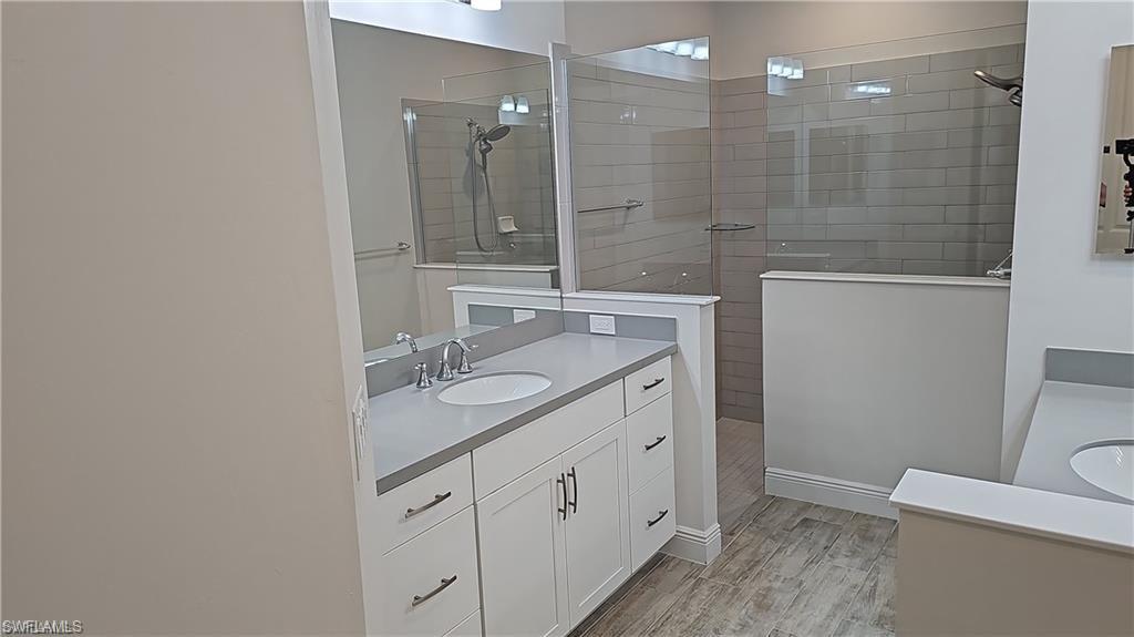Modern primary bathroom featuring a white vanity with dual drawers and chrome hardware, quartz countertop with integrated sink, polished chrome faucet, large framed mirror, and a frameless glass-enclosed shower with tile surround