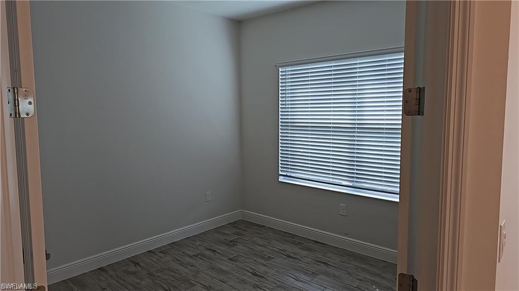Bright secondary bedroom featuring neutral gray walls, wood-finish flooring, and large window with horizontal blinds providing natural light and privacy control