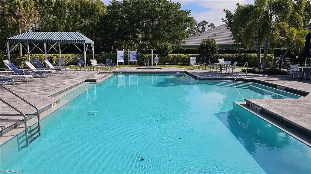 Community swimming pool with an integrated spa, paver deck, and covered lounging area