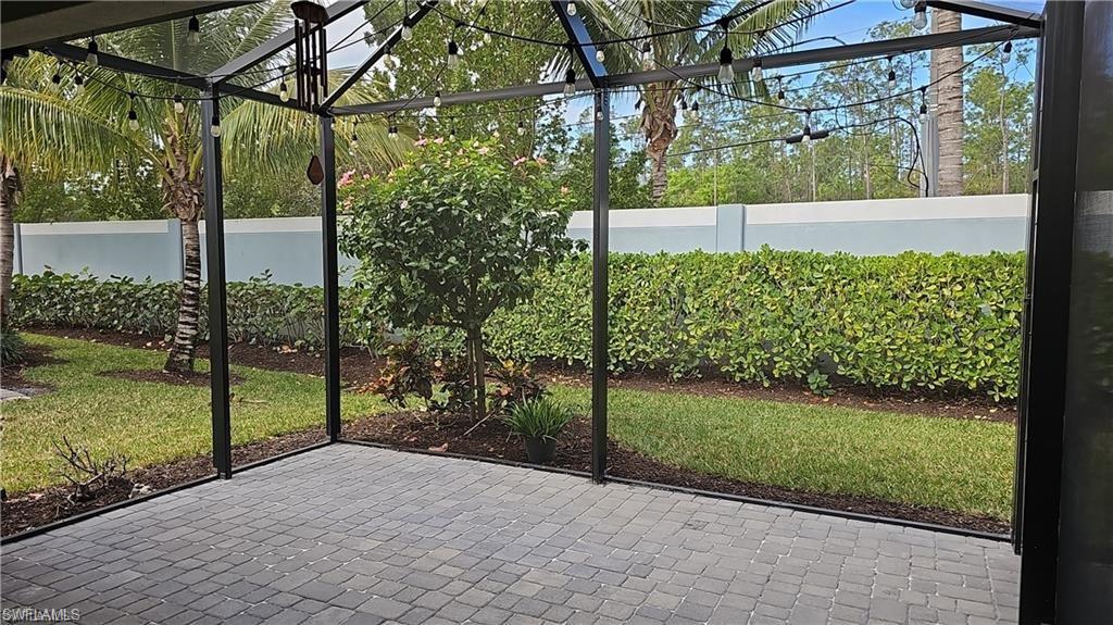 Screened patio featuring paver flooring, string lighting, and mature landscaping