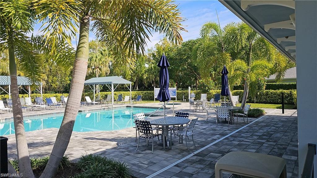 Resort-style poolside retreat featuring a sparkling saltwater pool, expansive paved terrace with multiple seating areas, mature palm trees providing natural shade, and retractable umbrellas for additional sun protection