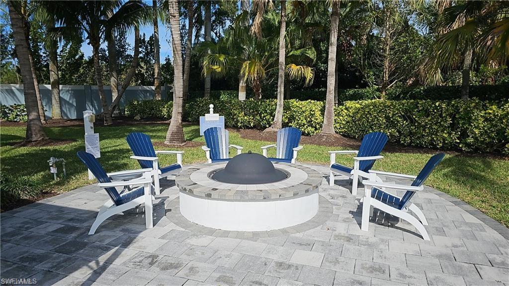 Paver patio with a stone and stucco fire pit, surrounded by lush landscaping and mature palm trees