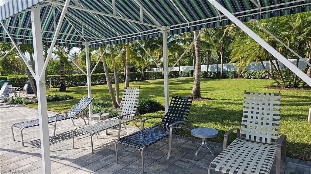 Striped canopy covering a paved patio, surrounded by a manicured lawn and mature palm trees