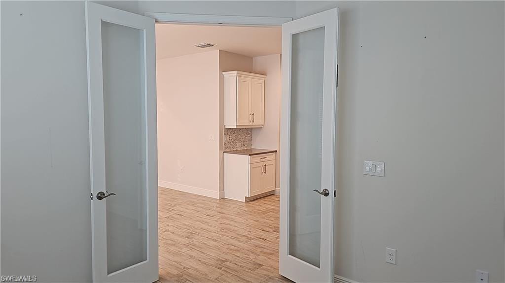 Double glass-paneled doors open to an interior space with wood-finish flooring, white cabinetry, and a mosaic tile backsplash
