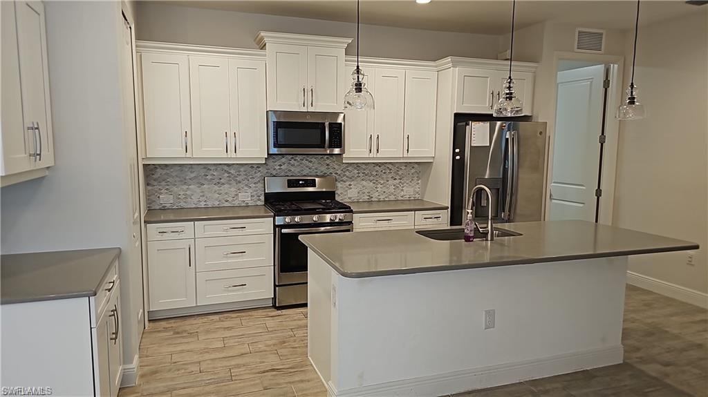 Kitchen featuring white shaker cabinetry, stainless steel appliances, a mosaic tile backsplash, and a center island with pendant lighting