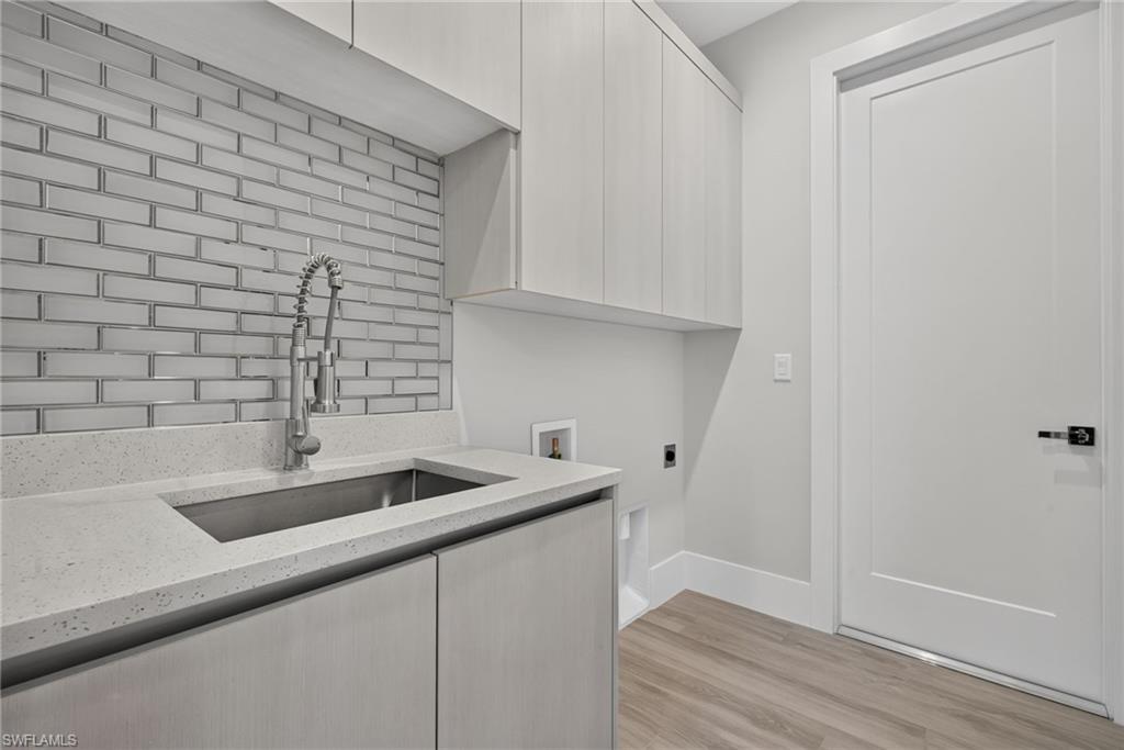 Built-in cabinetry, stainless steel undermount sink, commercial-style pull-down faucet, full-height subway tile backsplash, and wood-finish flooring