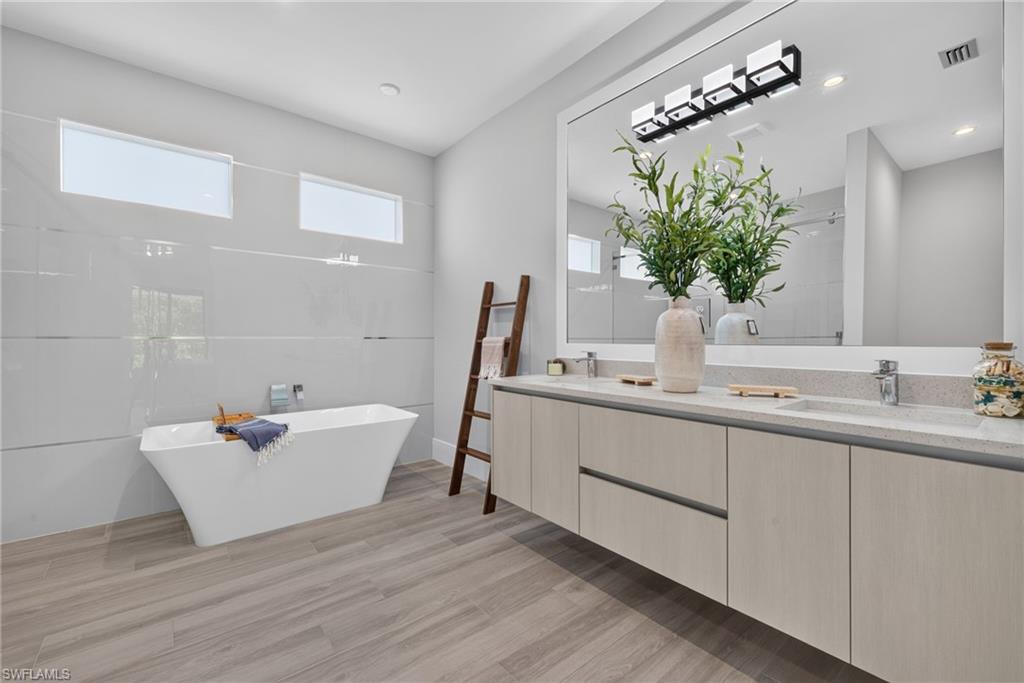 Floating double vanity with integrated sinks, large rectangular mirror, freestanding soaking tub, and wood-finish flooring