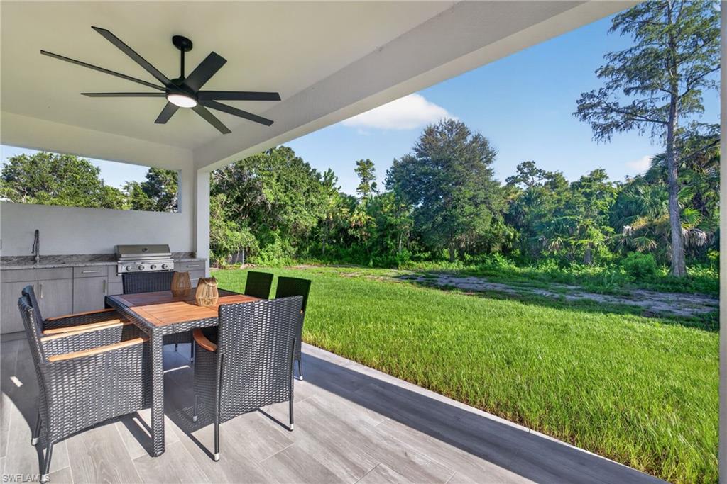 Covered patio with a multi-blade ceiling fan, built-in outdoor kitchen with a stainless steel grill, and wood-finish flooring
