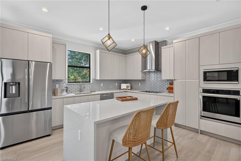 Contemporary kitchen featuring light wood-finish cabinetry, stainless steel appliances, a center island with a stone countertop, and a tile backsplash