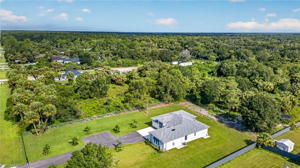 Expansive property featuring a modern residence with a light-colored exterior, a well-maintained lawn, and mature trees