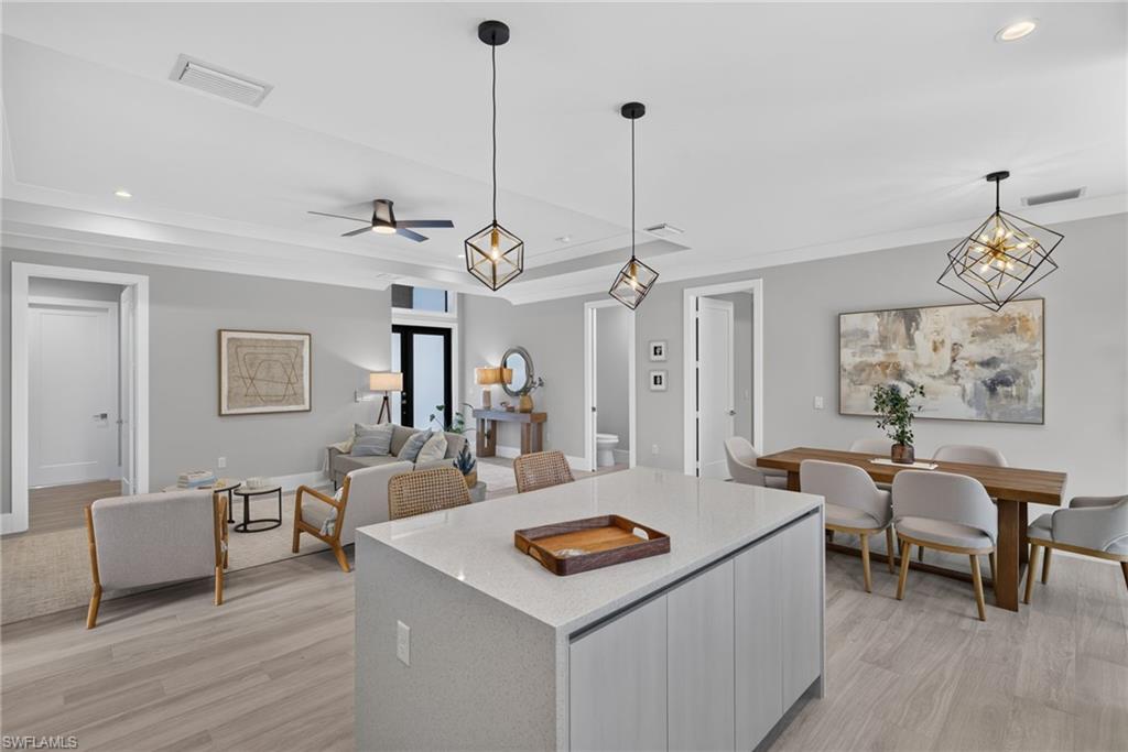 Expansive open-concept living area featuring wood-finish flooring, a kitchen island with a light-toned countertop, and crown molding