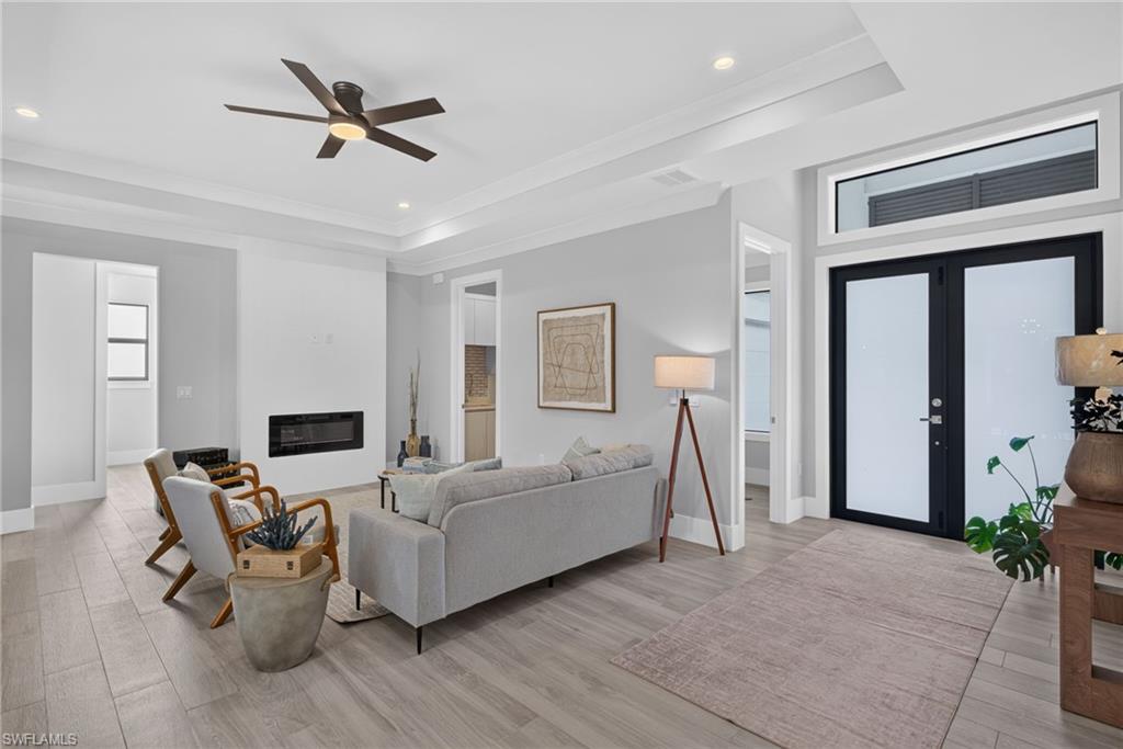 Tray ceiling with recessed lighting, linear fireplace, wood-finish flooring, and double entry doors with transom window
