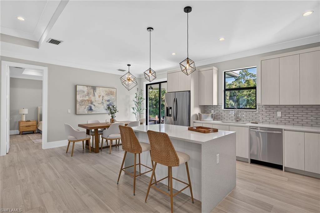 Contemporary kitchen with light wood-finish flooring, white cabinetry, integrated stainless steel appliances, a white island, and geometric pendant lighting
