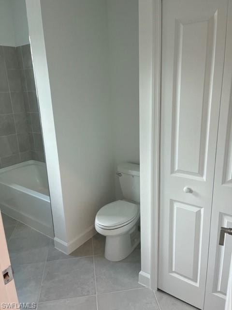 Bathroom with baseboards, toilet, tile patterned floors, and tub / shower combination