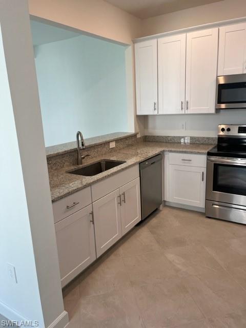 Kitchen with stove, dishwashing machine, a sink, white cabinets, and light stone counters