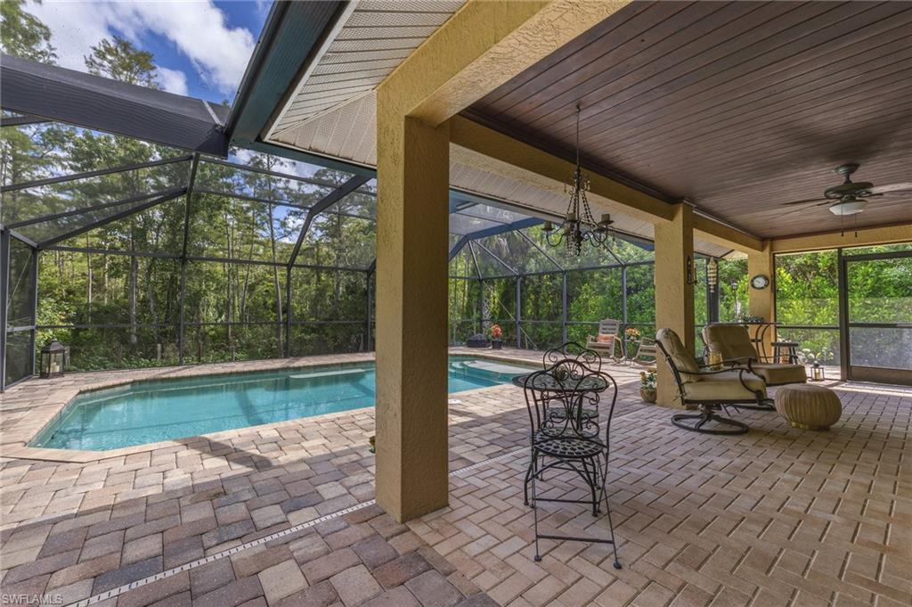 Screened lanai featuring a swimming pool, extensive paver decking, and a wood-finish ceiling with a chandelier and ceiling fan