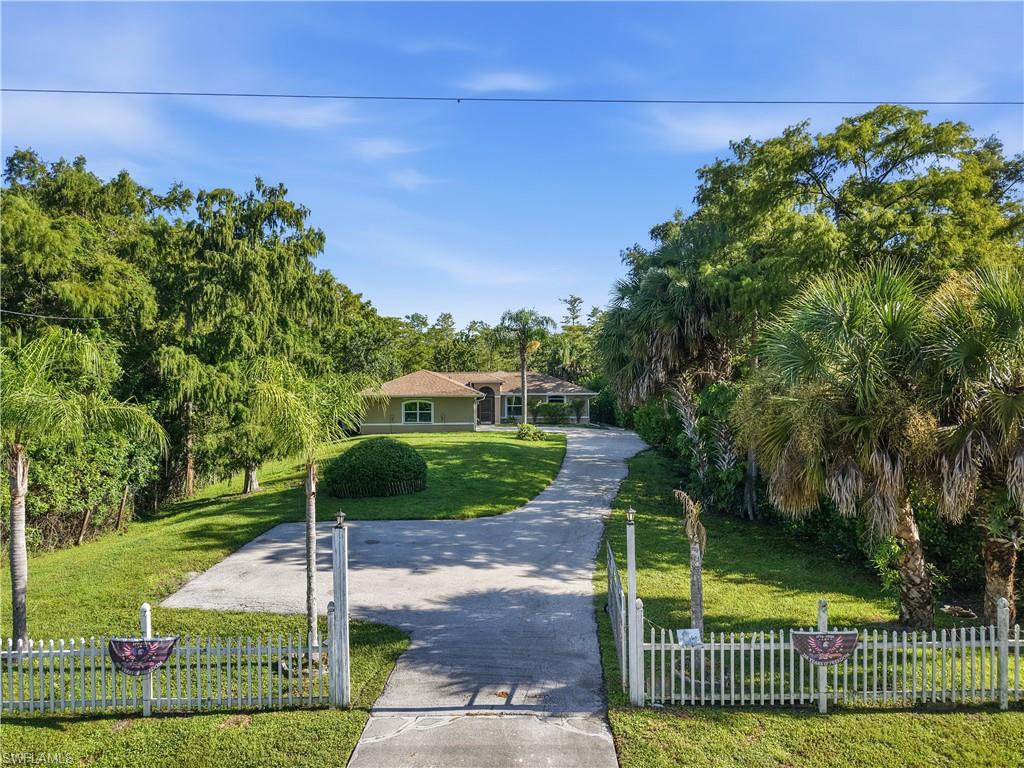 Gated entry with a white picket fence, a long paved driveway, and a well-maintained lawn