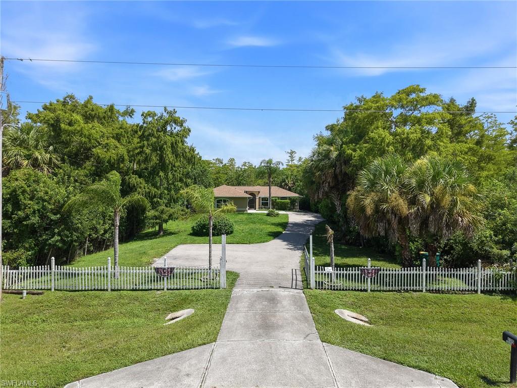 Gated entry with a white picket fence, concrete driveway, and lush surrounding landscaping