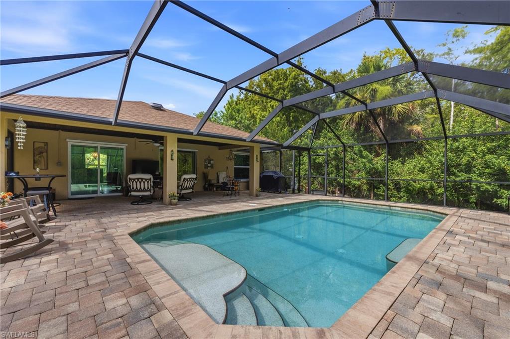 Screened pool enclosure featuring an in-ground swimming pool, paver patio, covered lanai, and sliding glass doors