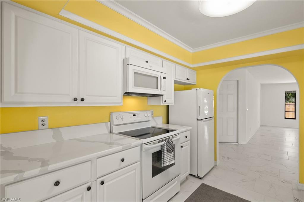 White cabinetry with dark hardware, solid surface countertops, white range, built-in microwave, and arched doorway