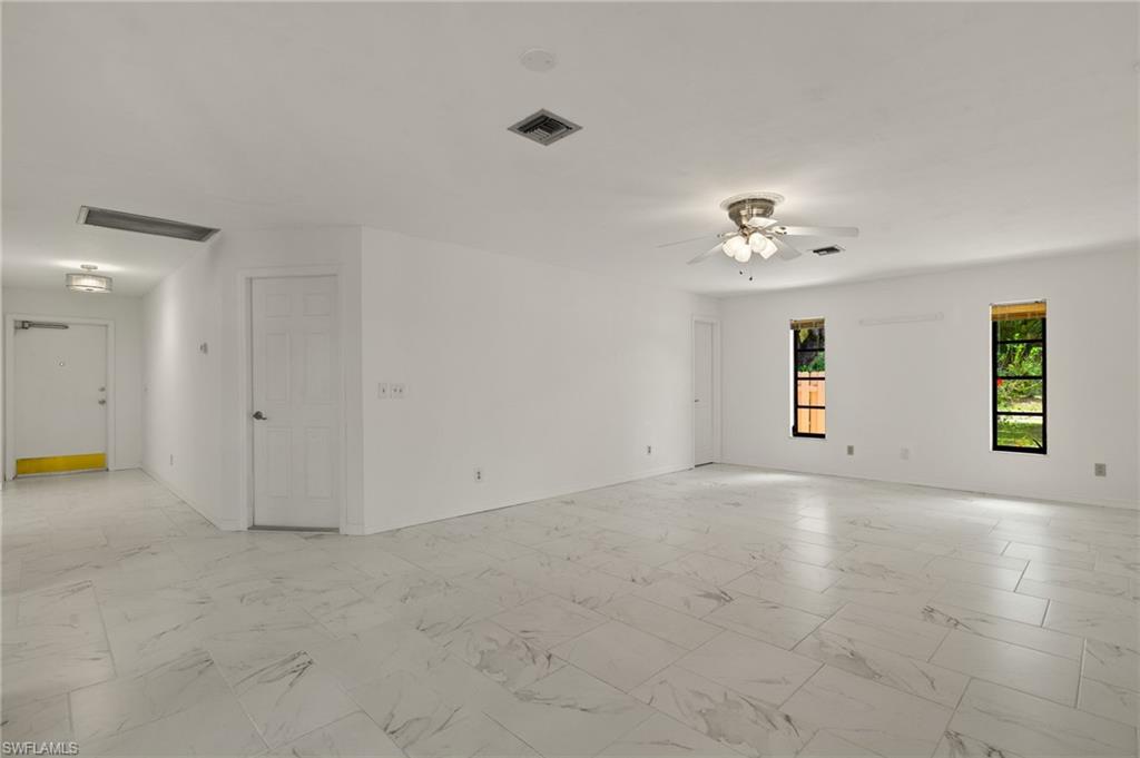 Spacious interior featuring large format tile flooring, multiple windows, a ceiling fan with integrated lighting, and recessed ceiling lighting