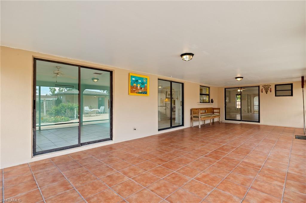 Expansive covered patio featuring terracotta-style tile flooring, ceiling-mounted light fixtures, and multiple sliding glass doors