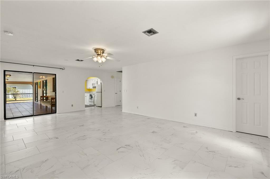Spacious open-concept room featuring marble-look tile flooring, bright white walls, and a ceiling fan with integrated lighting