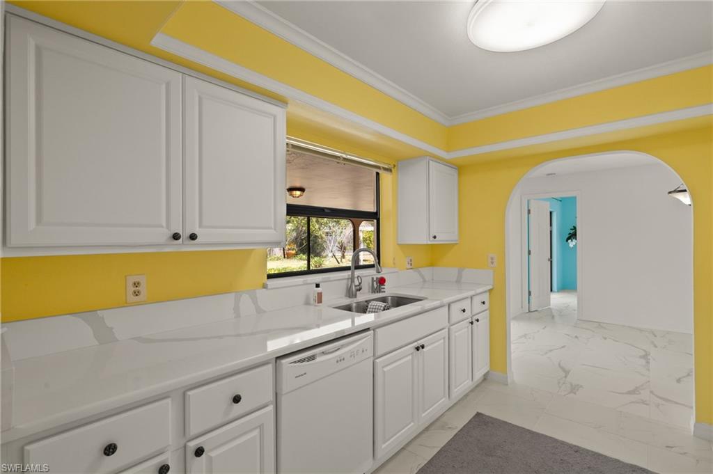 White cabinetry with dark hardware, stone-finish countertops, stainless steel sink with a gooseneck faucet, integrated dishwasher, and an arched doorway