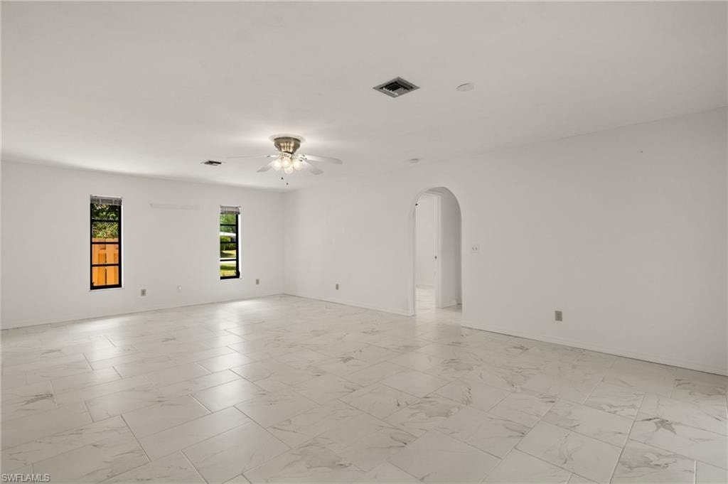 Spacious room featuring large format tile flooring, arched doorway, and ceiling fan with integrated lighting