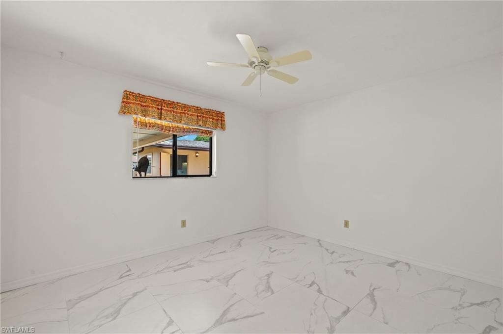 White walls with a ceiling fan light fixture and white marble-look tile flooring