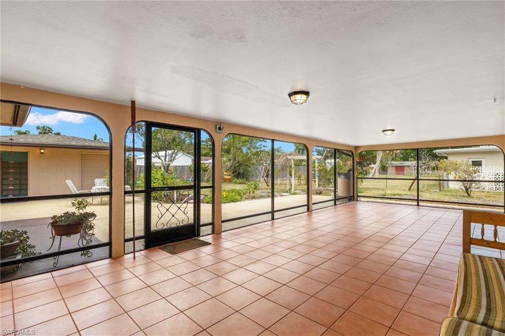 Screened enclosure featuring a tile floor, multiple windows, a full-light entry door, and ceiling-mounted light fixtures