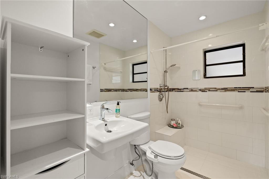Built-in shelving, full-height mirrored wall, single-handle faucet, tiled shower with integrated bench, and mosaic tile accent band