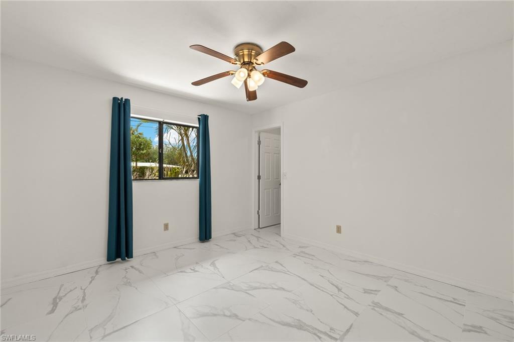 Spacious room featuring large format tile flooring with subtle veining, a ceiling fan with integrated lighting, and a window offering natural illumination