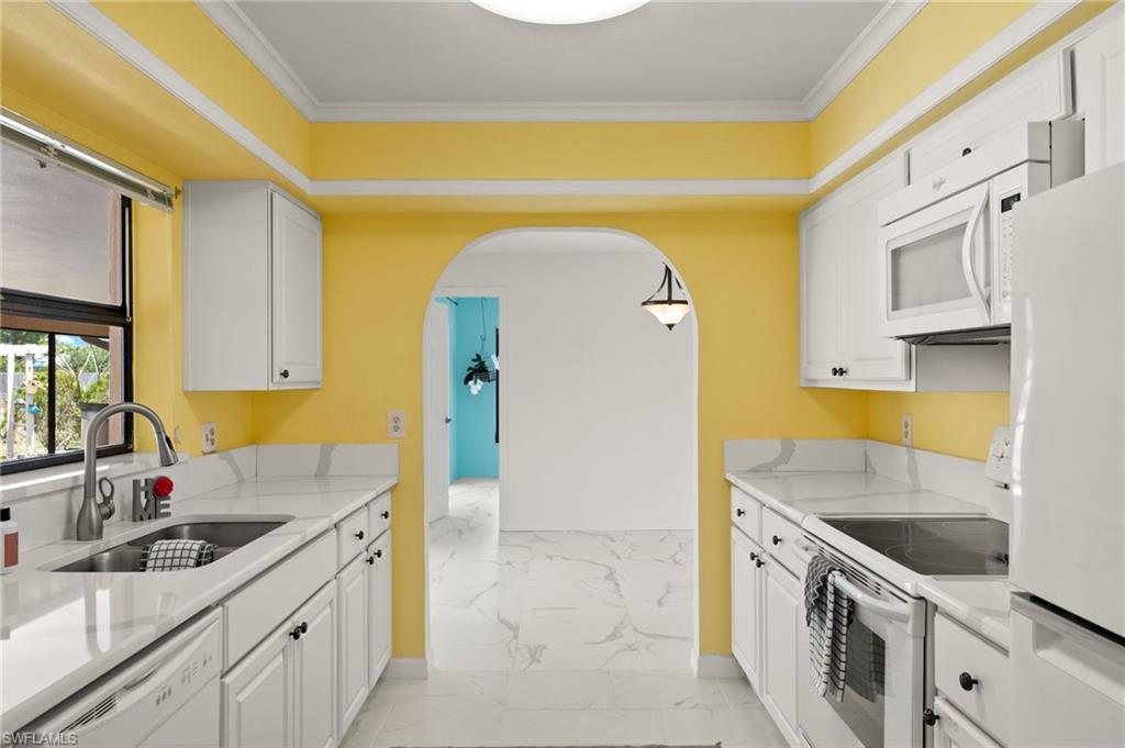 White cabinetry with dark hardware, stone-finish countertops, stainless steel sink with a gooseneck faucet, white built-in appliances, and arched doorway