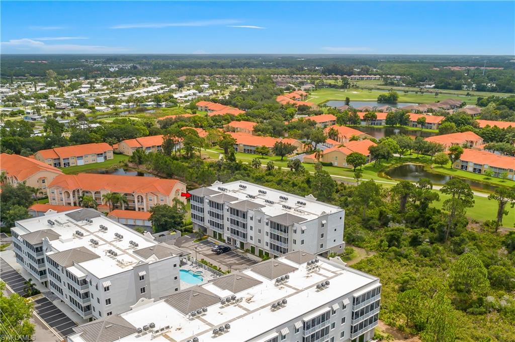 Condominium complex featuring a communal swimming pool, surrounding parking areas, and mature landscaping, with a golf course and ponds in the background