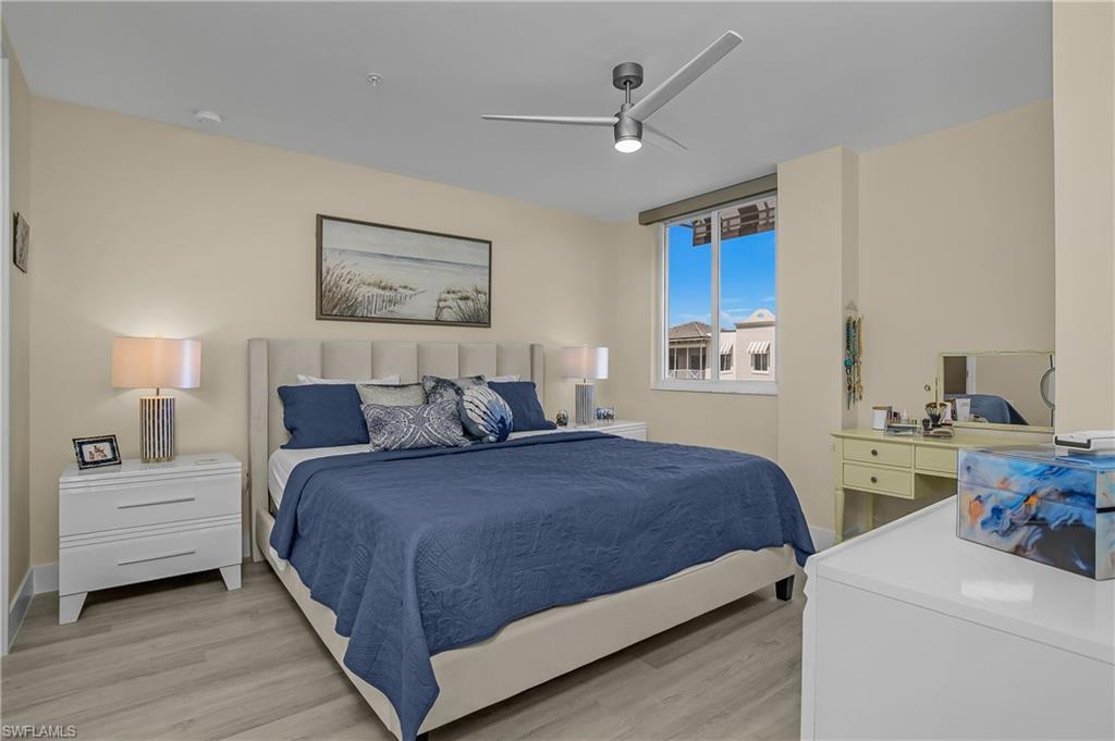 Light-toned walls, wood-finish flooring, a contemporary ceiling fan, and a large window with roller shades