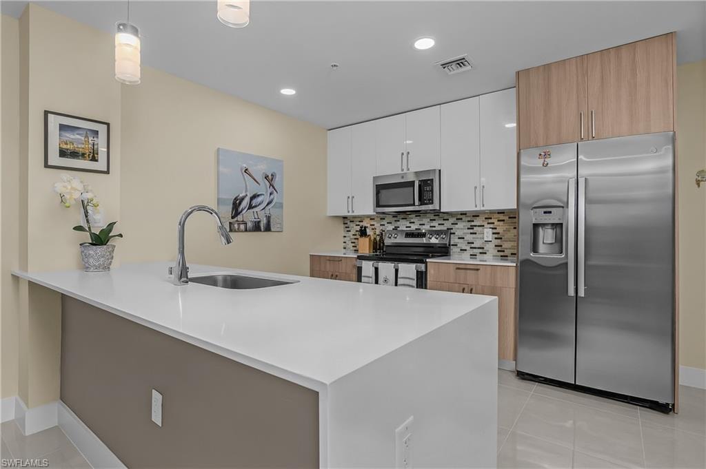 Contemporary kitchen featuring a large island with an integrated sink, stainless steel appliances, two-tone cabinetry, a tile backsplash, and recessed lighting
