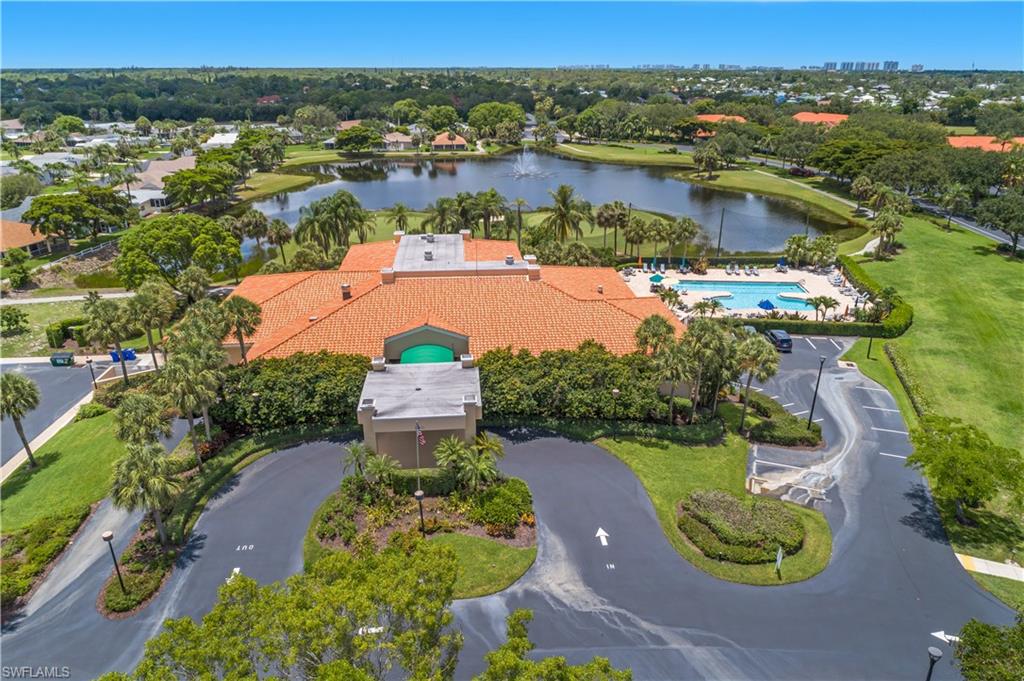 Community building with a terracotta-tiled roof, a resort-style swimming pool, and an expansive paved parking area