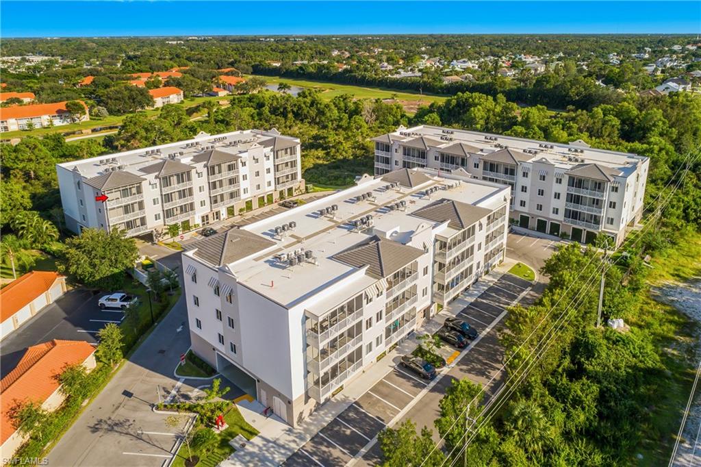Contemporary multi-story buildings featuring screened balconies, flat roofs with gabled accents, and a surrounding of lush greenery