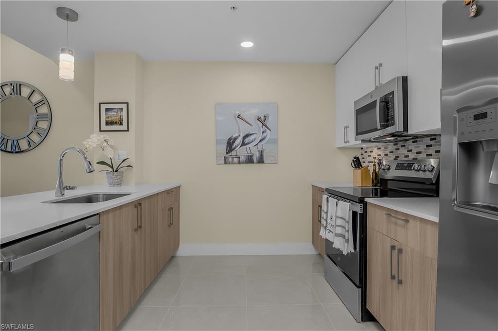 Sleek kitchen featuring stainless steel appliances, a tile backsplash, light wood-finish cabinetry, and recessed lighting