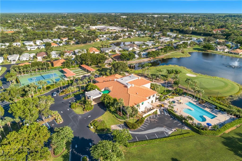 Clubhouse with a red tile roof, an adjacent swimming pool, tennis courts, a golf course, and a large pond with a fountain
