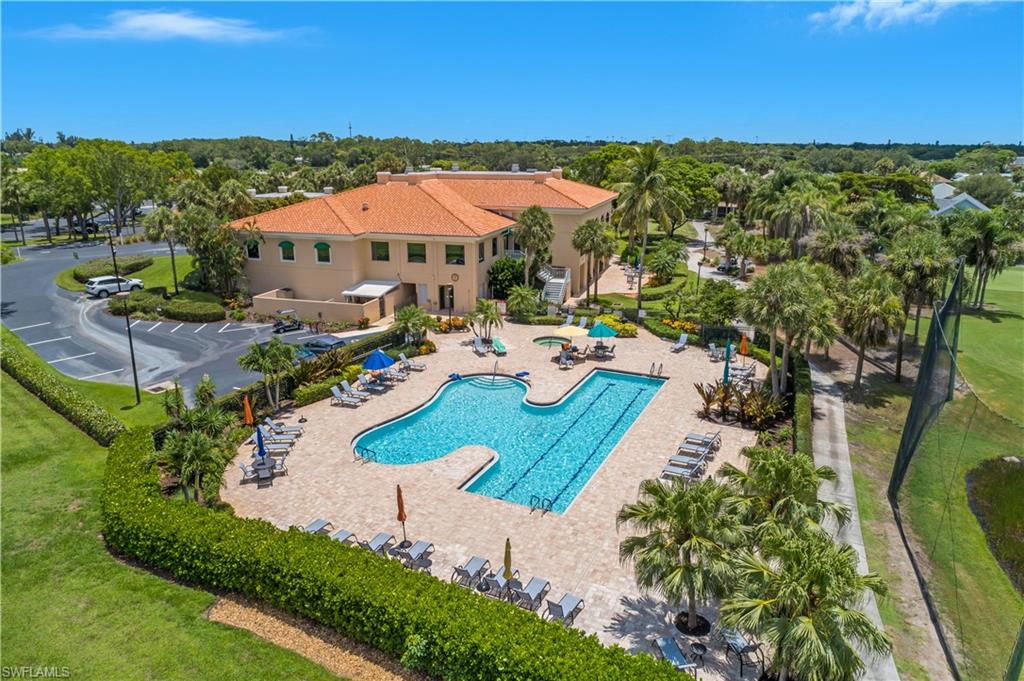 Central building with a tile roof, an expansive outdoor pool, paved pool deck, lush landscaping, and surrounding green spaces