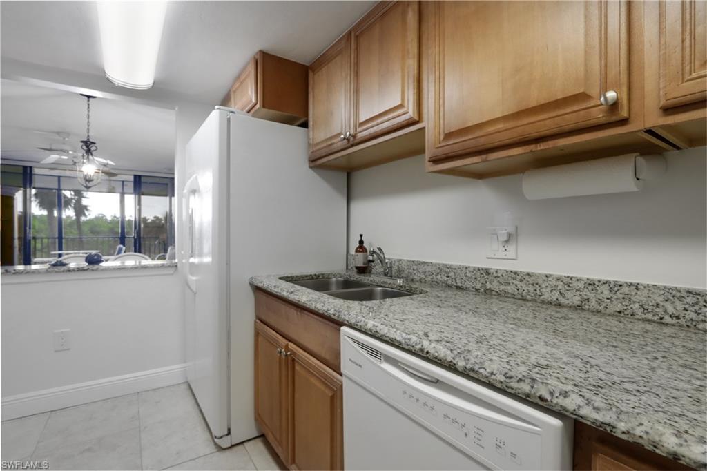 Kitchen with dishwasher, a sink, light stone countertops, light tile patterned flooring, and brown cabinetry