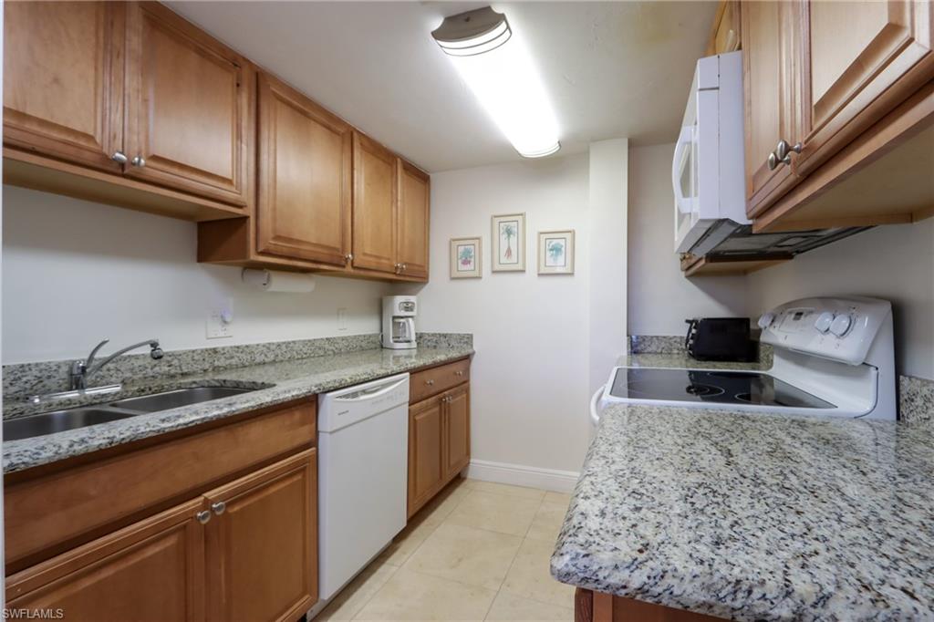 Kitchen featuring white appliances, a sink, brown cabinets, baseboards, and light stone counters