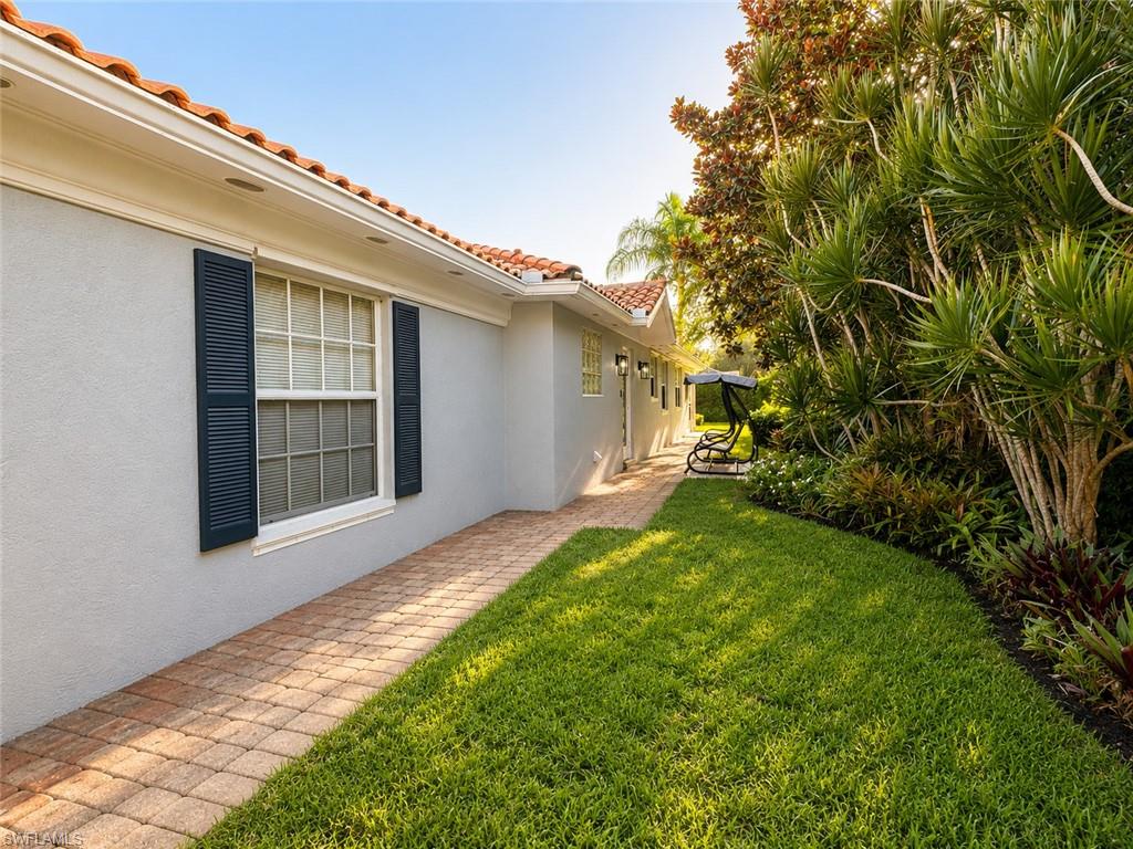 Charming single-story residence featuring a brick paver pathway, manicured lawn, and mature tropical landscaping including native palms