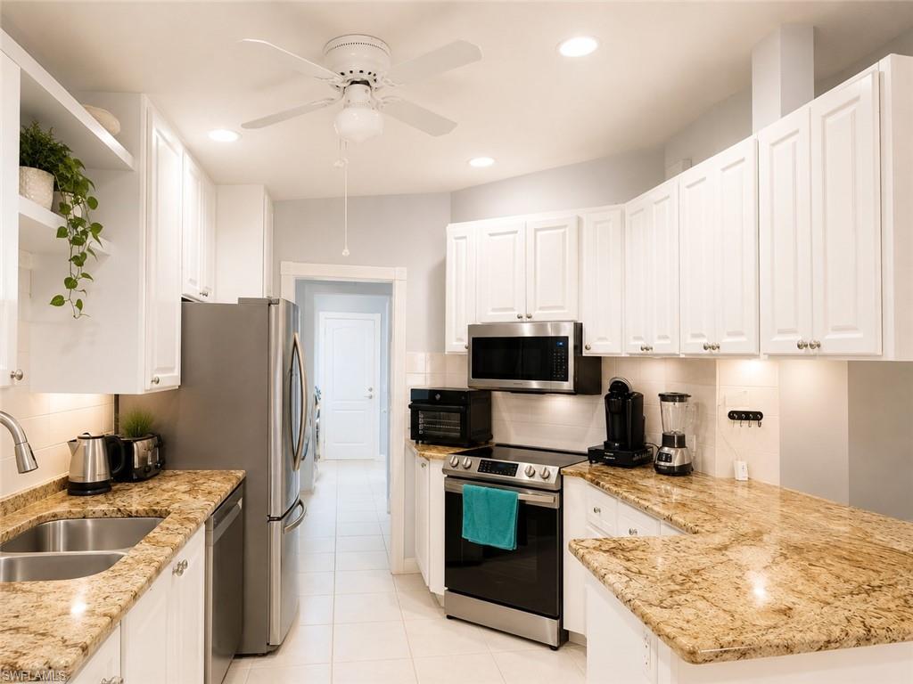 Kitchen featuring extensive white cabinetry, stainless steel appliances, light-toned stone countertops, a double basin stainless steel sink, and recessed lighting