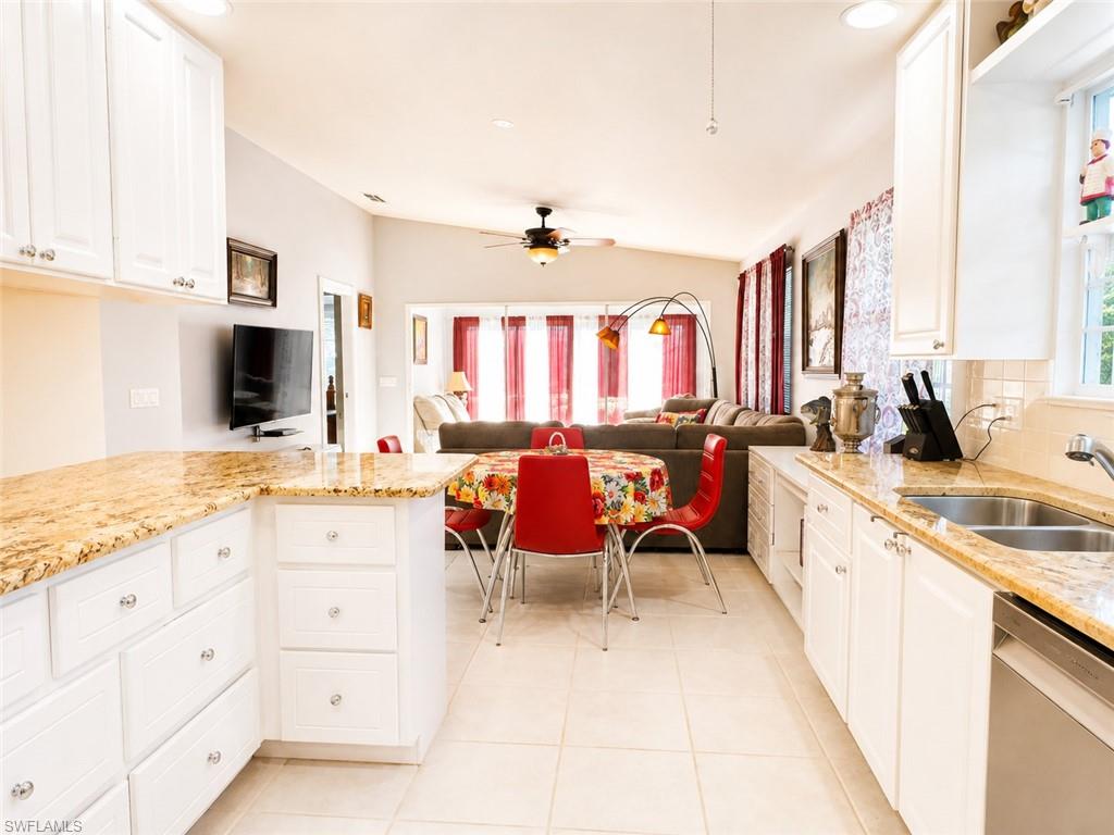 Open-concept kitchen and dining area featuring white cabinetry with hardware accents, granite-finish countertops, stainless steel appliances including a dishwasher and undermount sink, ceramic tile flooring, and abundant natural light from multiple windows